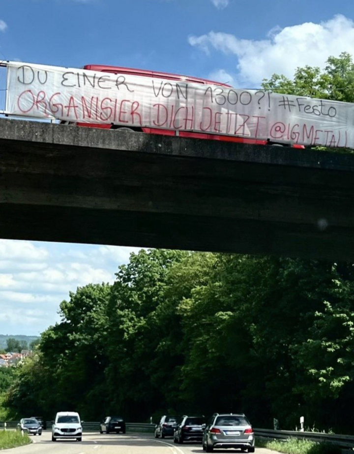 Protest Banner an Autobahnbrücke mit der Aufschrift "Du einer von 1300? #Festo ORGANISIER DICH JETZT @IGMETALL"